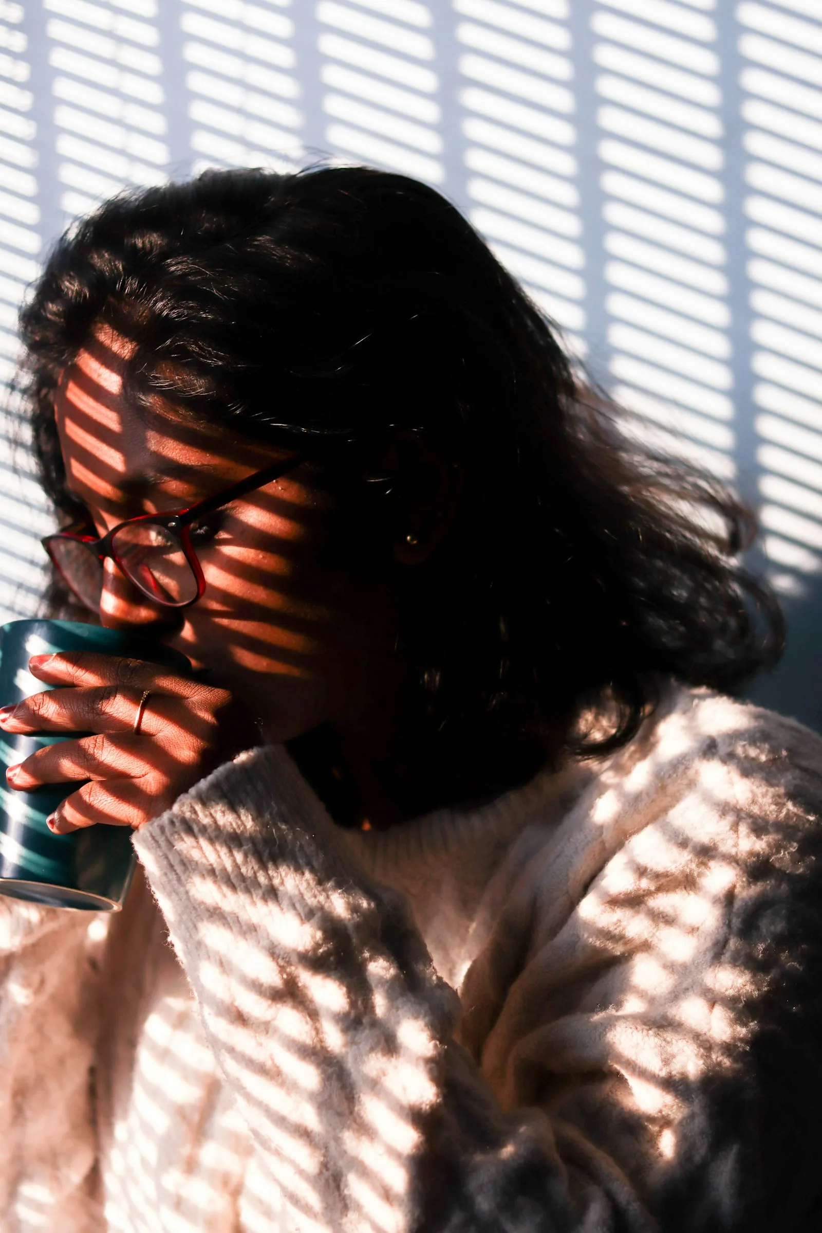 A woman in a cream sweater sipping tea in striped morning light